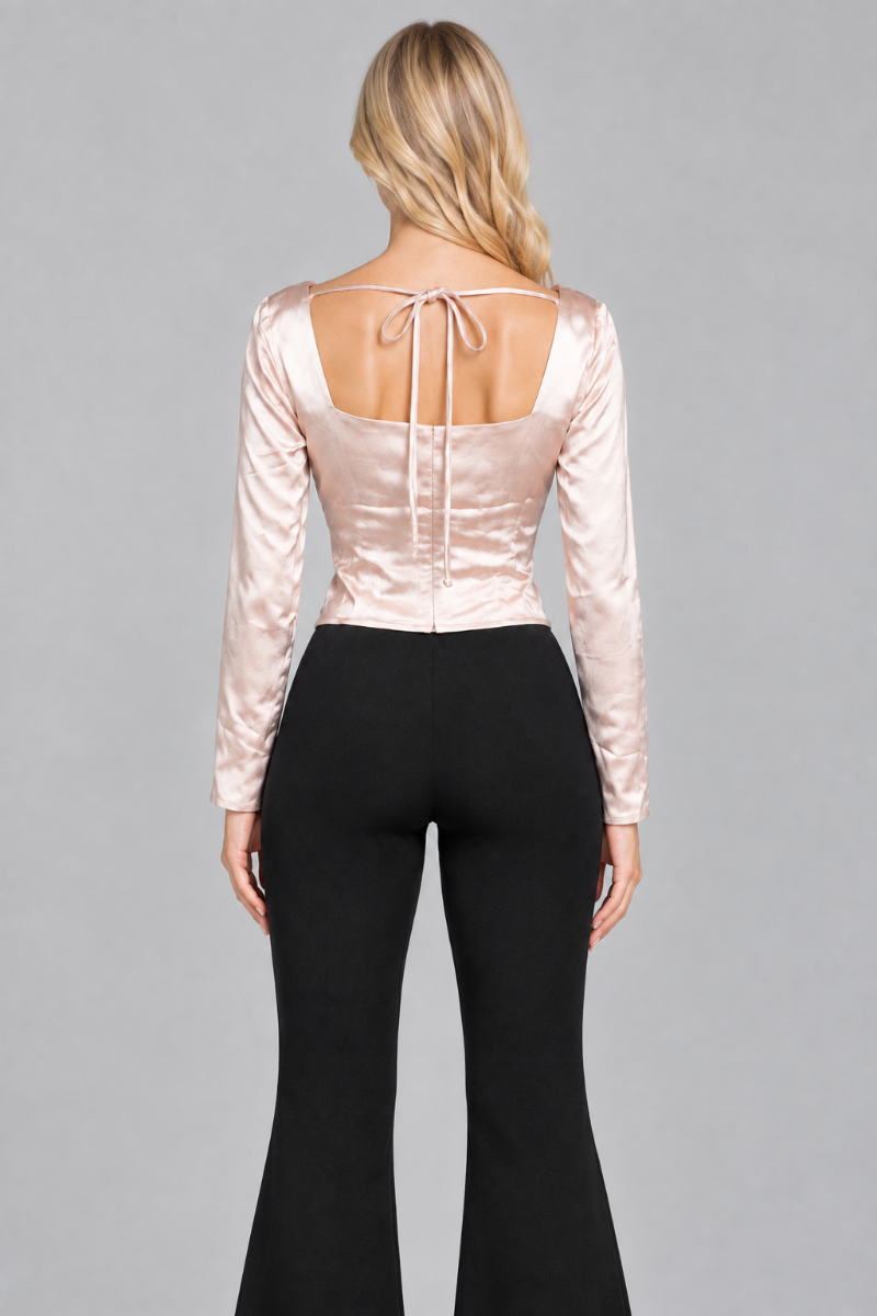 Back studio view of the blonde model wearing the champagne satin top with its open back, bow ties, and black flared trousers