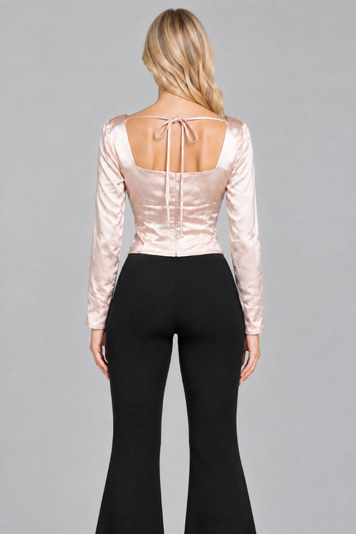 Back studio view of the blonde model wearing the champagne satin top with its open back, bow ties, and black flared trousers