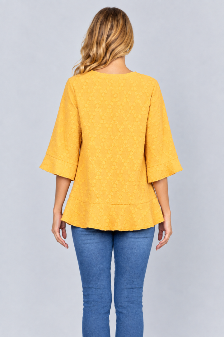Back studio view of the blonde model wearing the mustard-yellow textured blouse and blue jeans