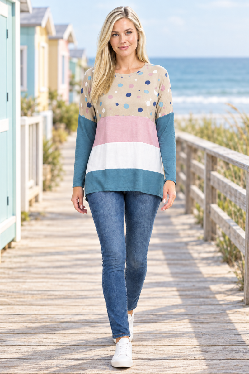 Full-body front view of blonde model in taupe dotted color-block tunic and jeans on a coastal boardwalk