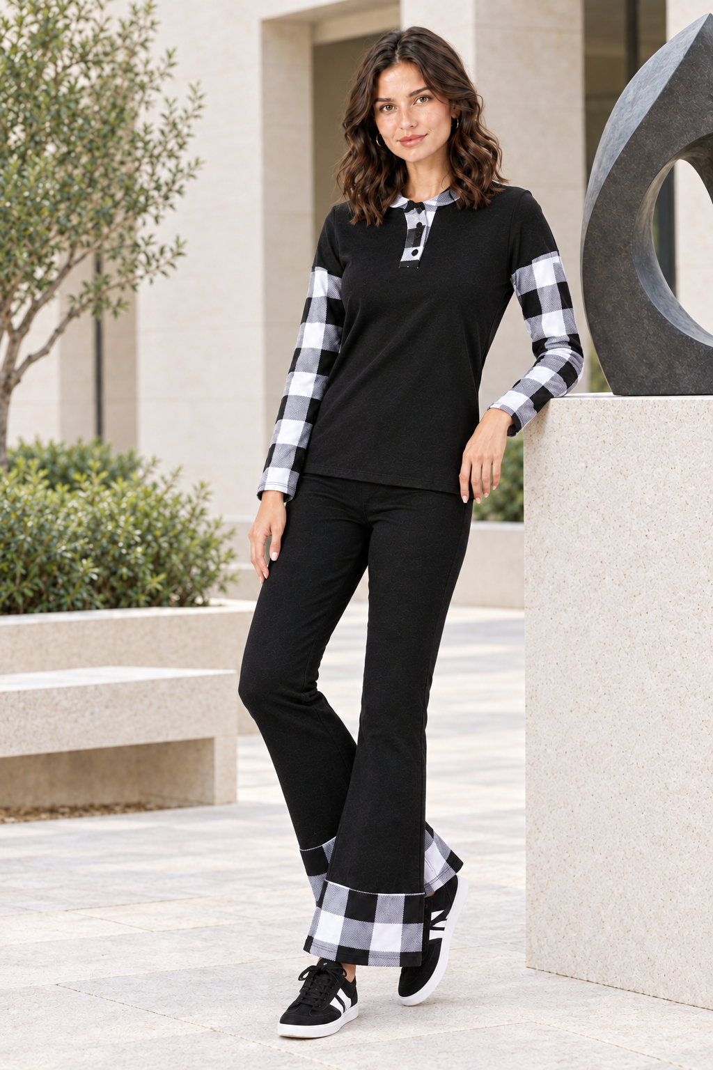 Full-body half-side lifestyle view, black outfit with black-and-white plaid accents, sculpture courtyard