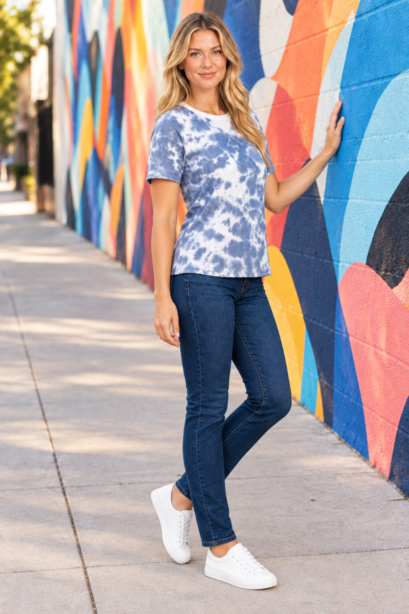 Full-body half-side lifestyle view, blonde model in blue-and-white tie-dye top and jeans, mural background