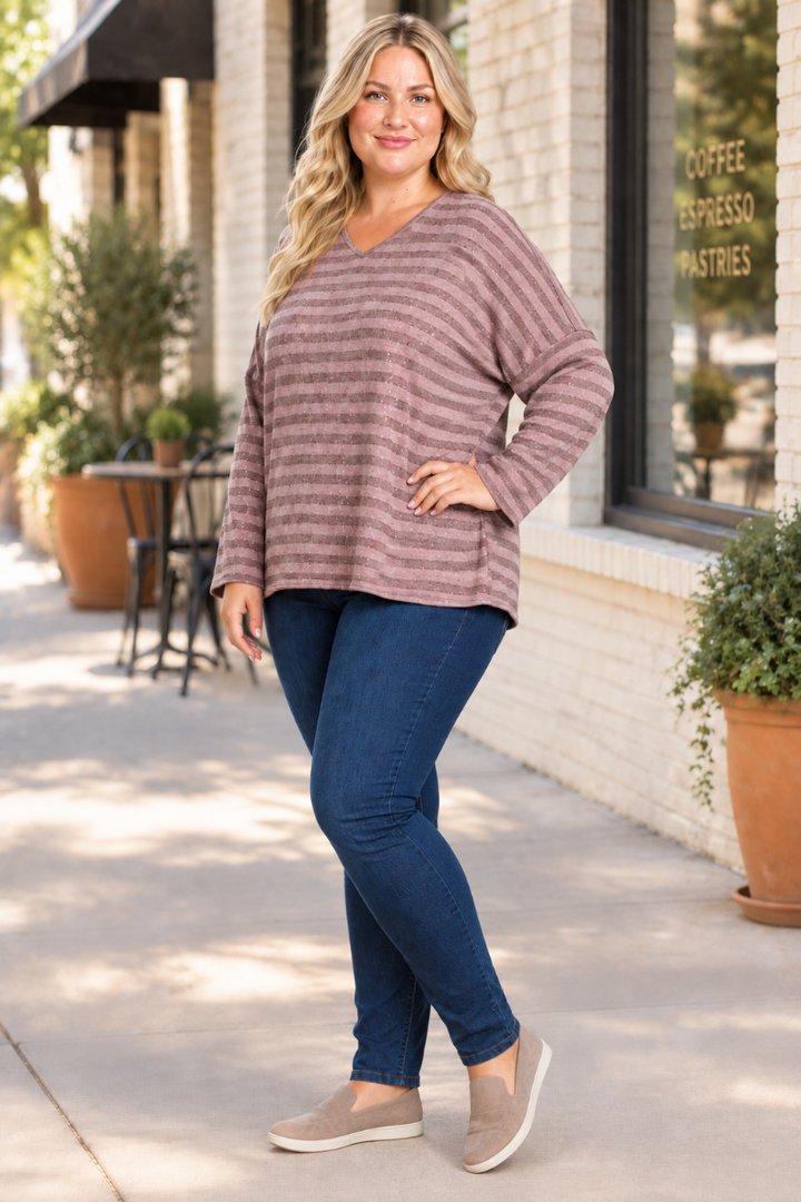 Full-body half-side lifestyle view, blonde plus-size model in mauve striped top and dark jeans