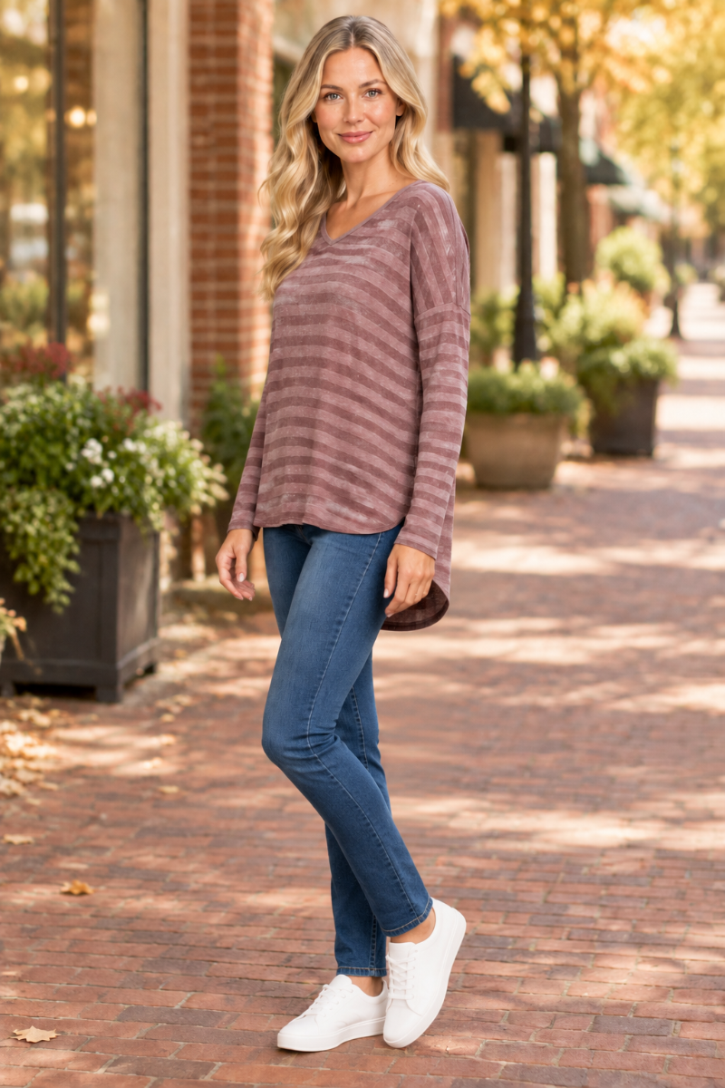 Full-body half-side lifestyle view of the blonde model wearing the mauve striped top, blue jeans, and white sneakers