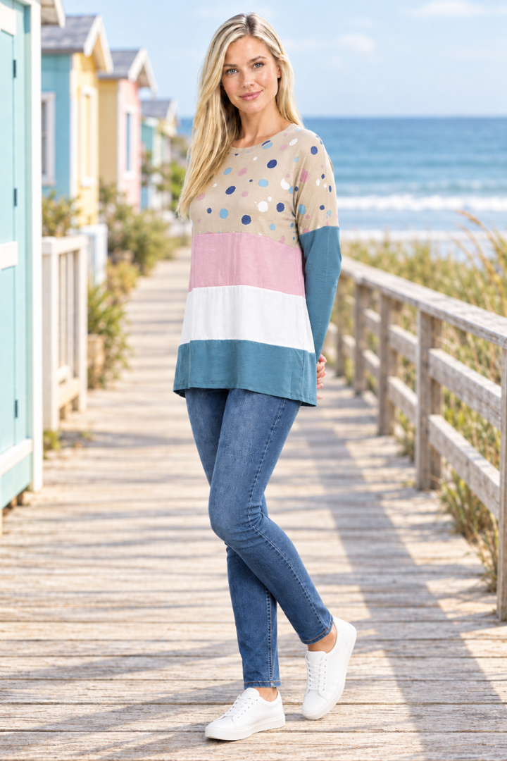 Full-body half-side view of blonde model in taupe dotted color-block tunic and jeans on a coastal boardwalk