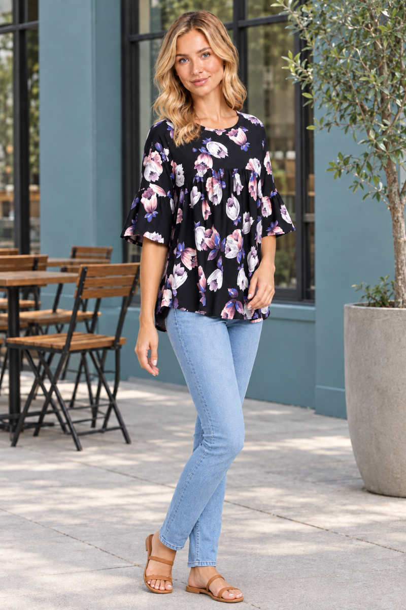 Full-body half-side view of the blonde model wearing the floral blouse and light-wash jeans on a café terrace
