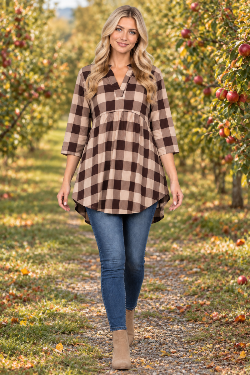 Full-body lifestyle front view of a blonde model wearing the beige-and-brown plaid tunic, jeans, and tan boots in an apple orchard