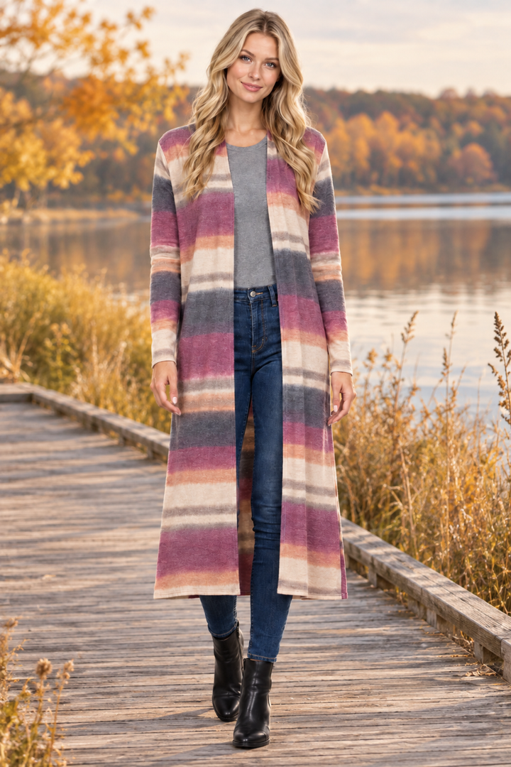Full-body lifestyle front view of a blonde model wearing the striped cardigan, gray top, jeans, and black boots by an autumn lake