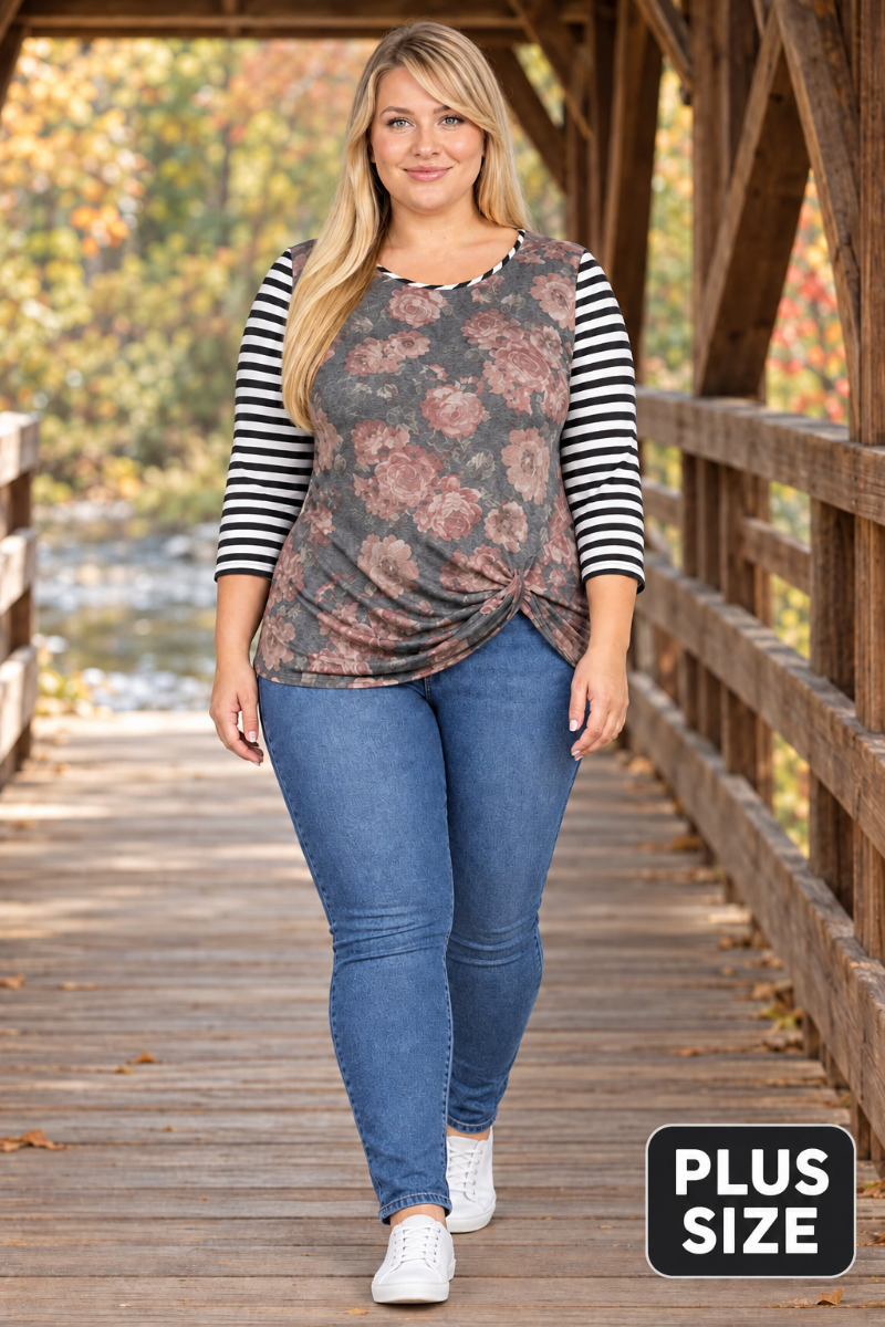 Full-body lifestyle front view of blonde model in charcoal floral top with striped sleeves and blue jeans on a covered bridge