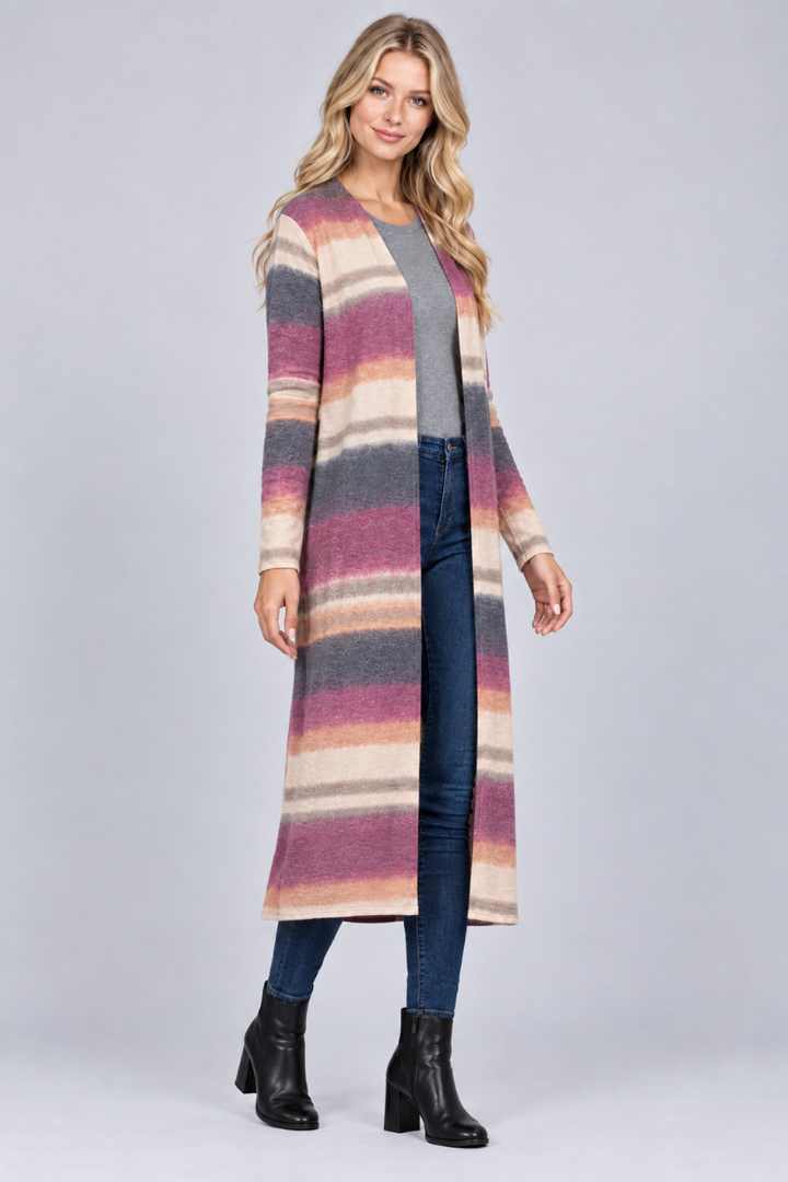 Full-body three-quarter studio view of a blonde model wearing the long striped cardigan, gray top, jeans, and black boots