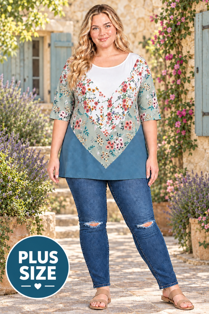 Full-body view of the blonde plus-size model in the sage-and-teal floral tunic against a lavender courtyard background