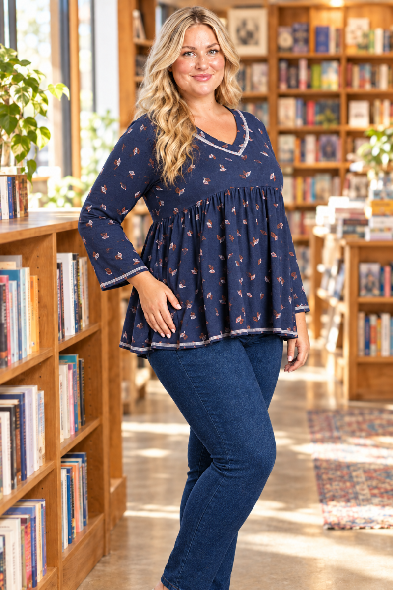 Half-side lifestyle view of blonde model in navy leaf-print blouse with contrast trim, bookstore setting