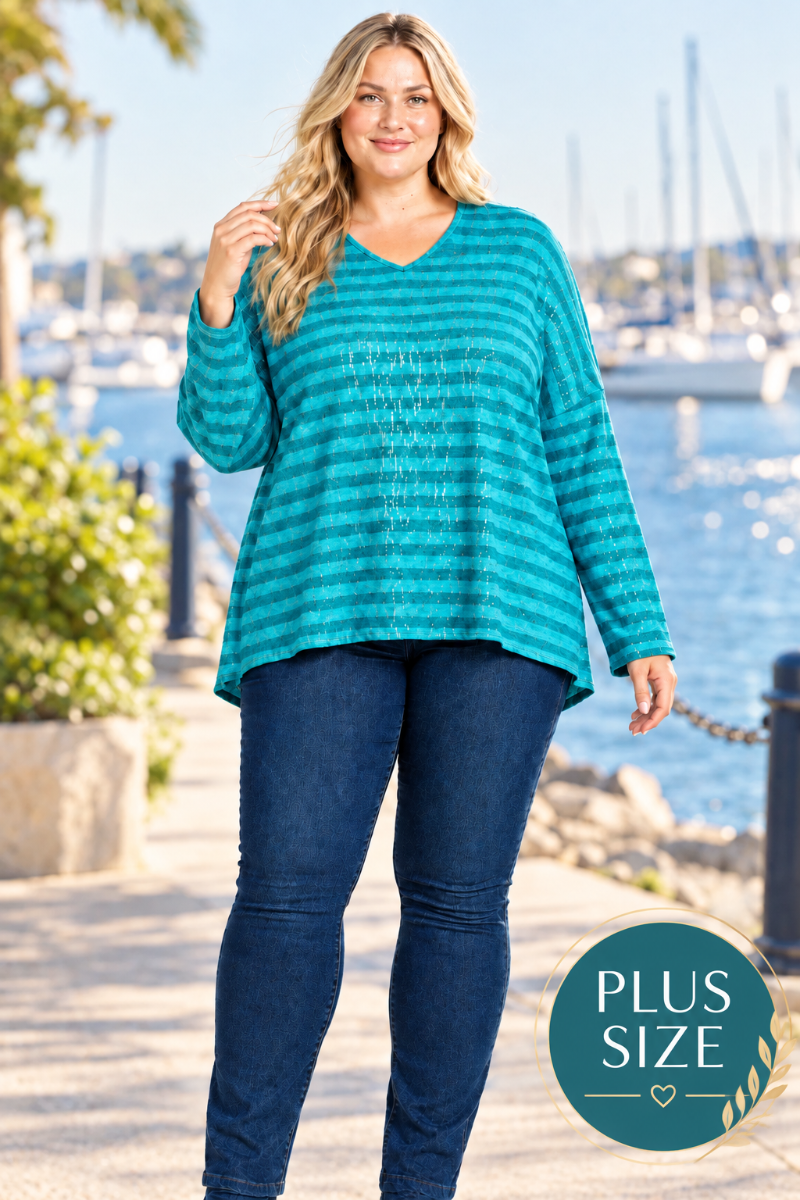 Lifestyle front view of blonde model in a loose teal striped top and dark jeans, harbor background