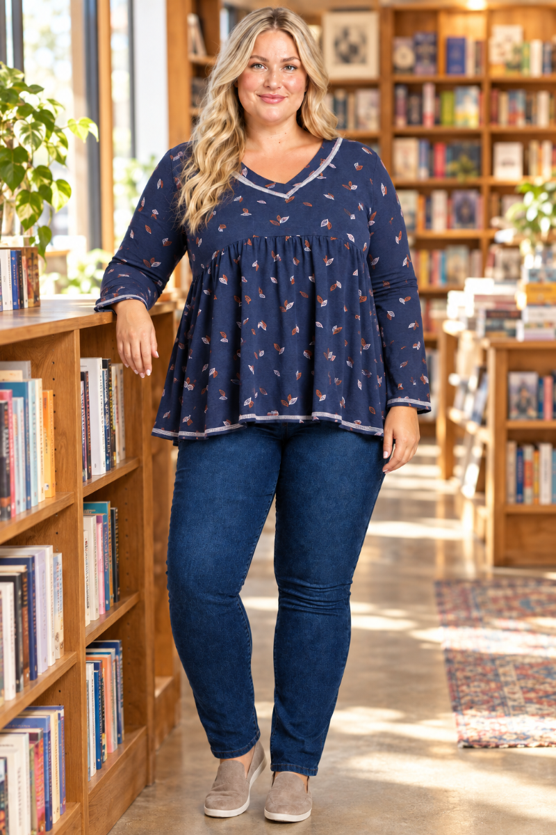 Lifestyle front view of blonde model in navy leaf-print blouse with contrast trim, bookstore setting