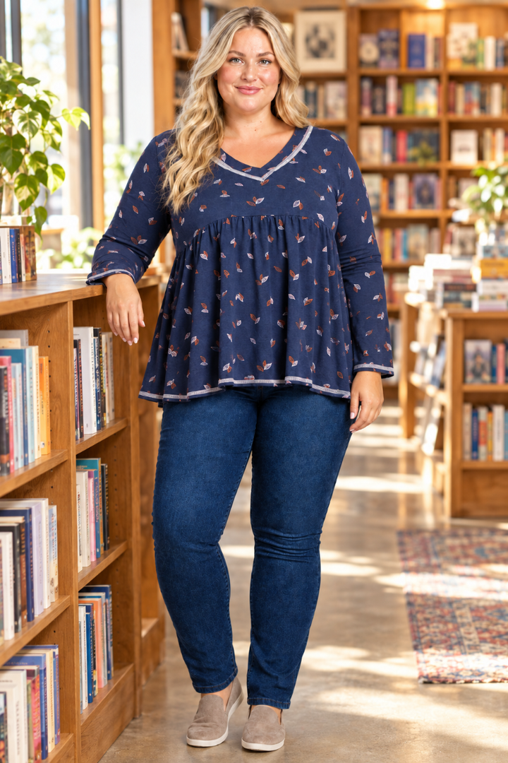 Lifestyle front view of blonde model in navy leaf-print blouse with contrast trim, bookstore setting