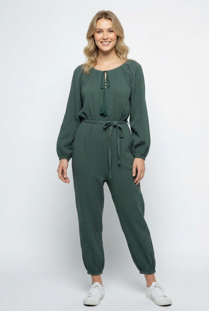 Smiling regular-size blonde model wearing the forest-green jumpsuit and white sneakers