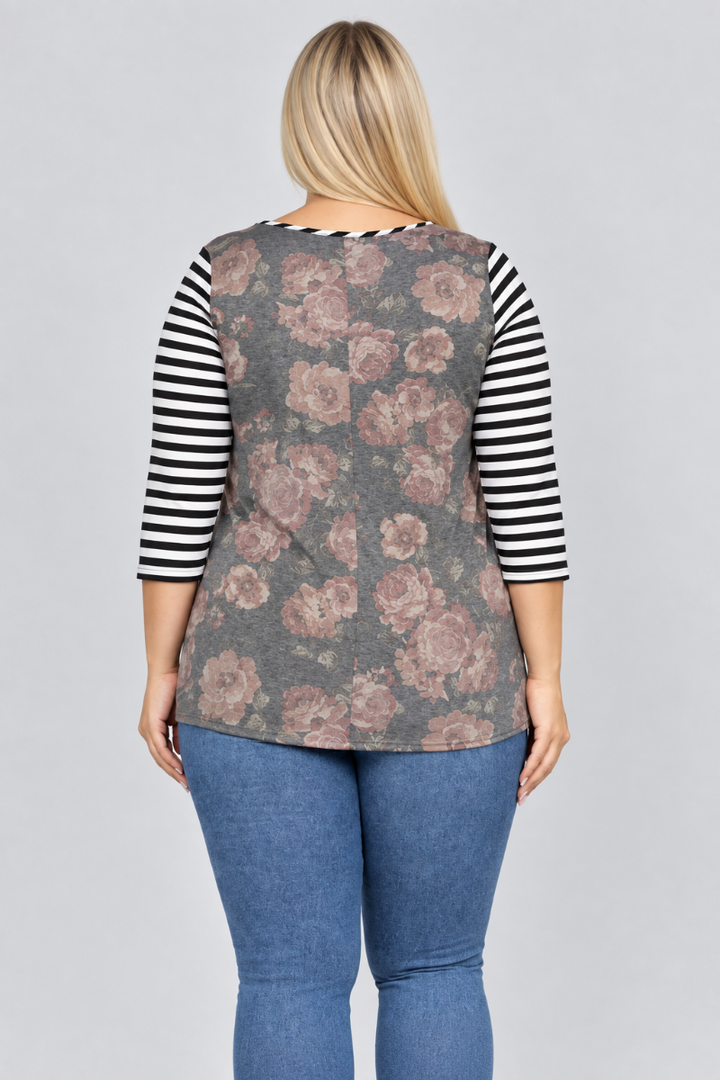 Studio back view of blonde model in charcoal floral top with black-and-white striped sleeves and blue jeans