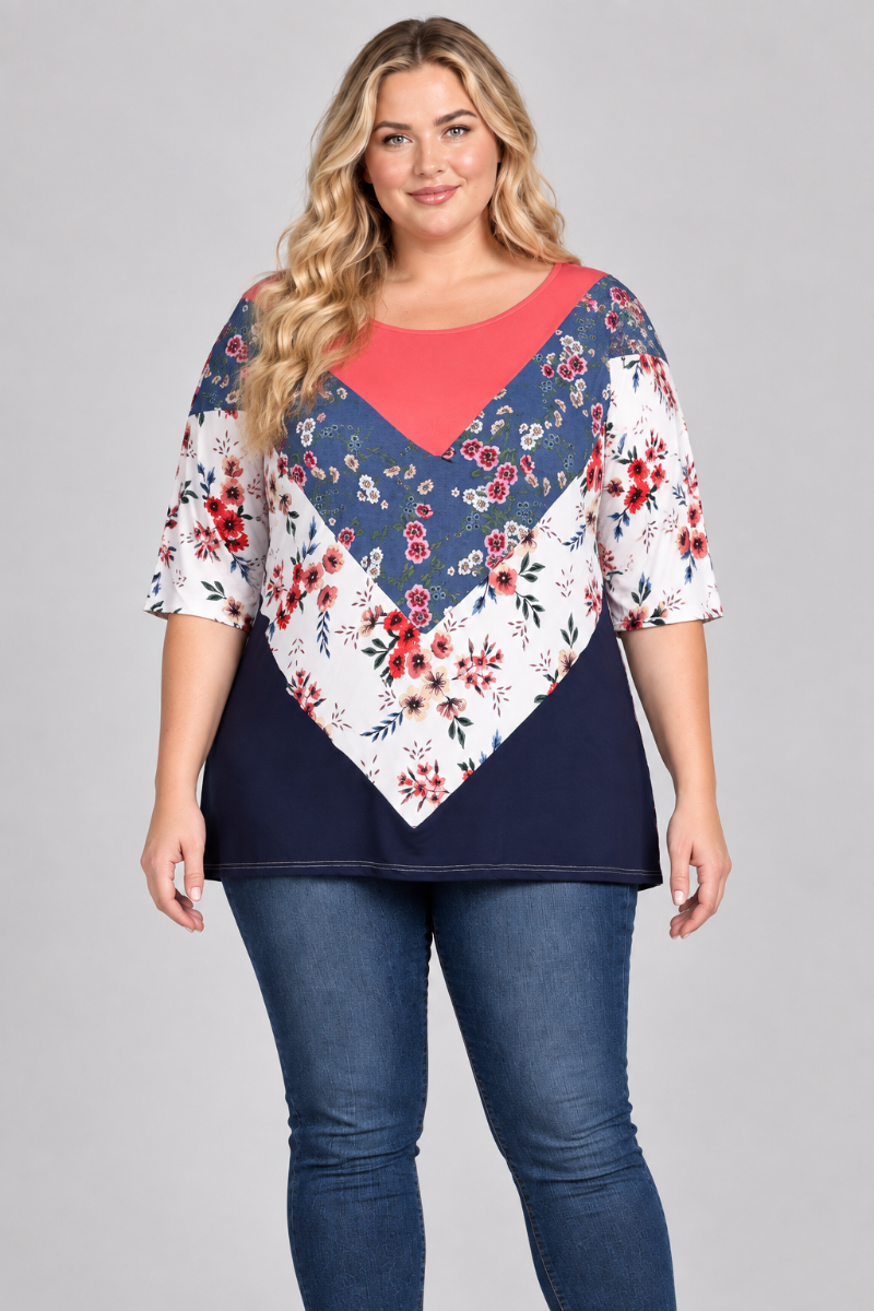 Studio front view of a new blonde plus-size model wearing the coral, blue, and white floral color-block top with blue jeans