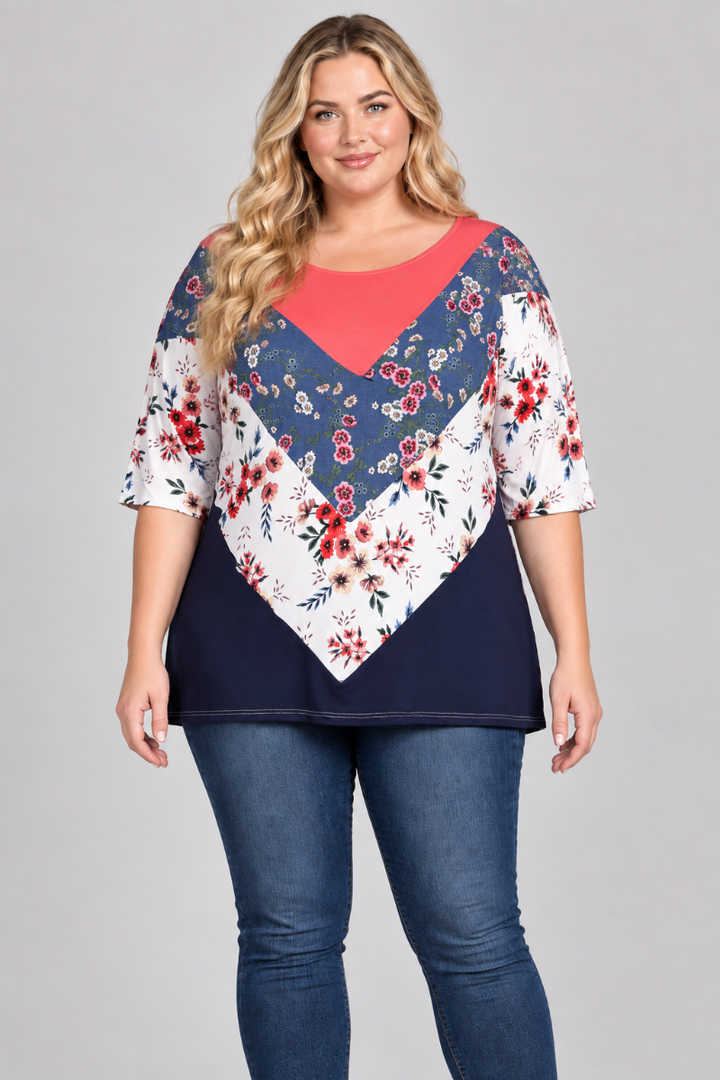 Studio front view of a new blonde plus-size model wearing the coral, blue, and white floral color-block top with blue jeans
