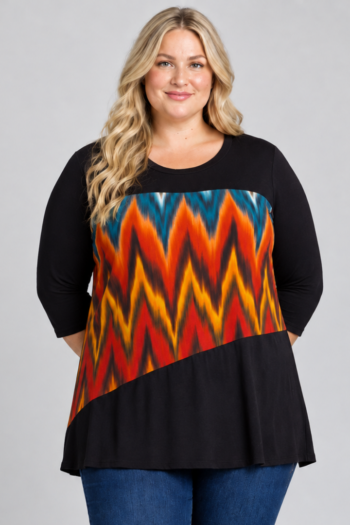 Studio front view of blonde model in black tunic with teal, orange, yellow, and red geometric panel and dark jeans