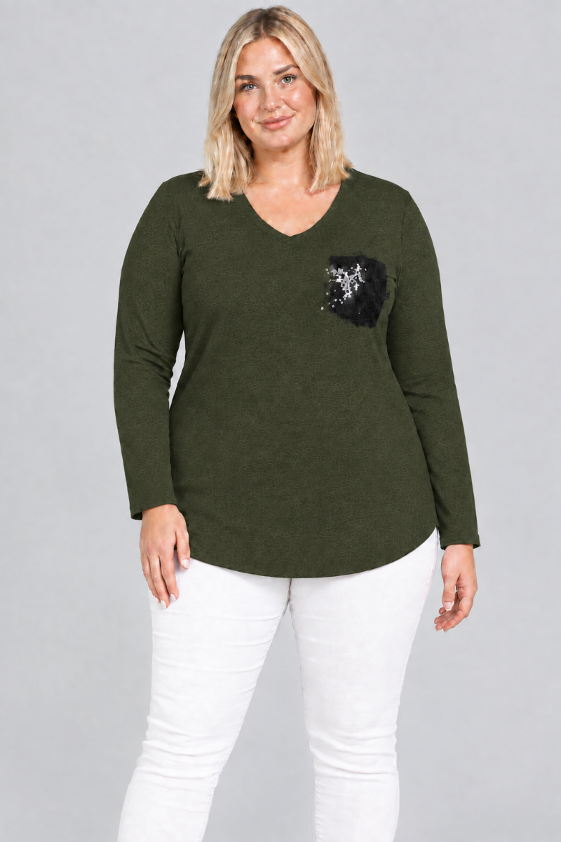 Studio front view of blonde model in dark olive V-neck tunic with black embellished pocket and white pants