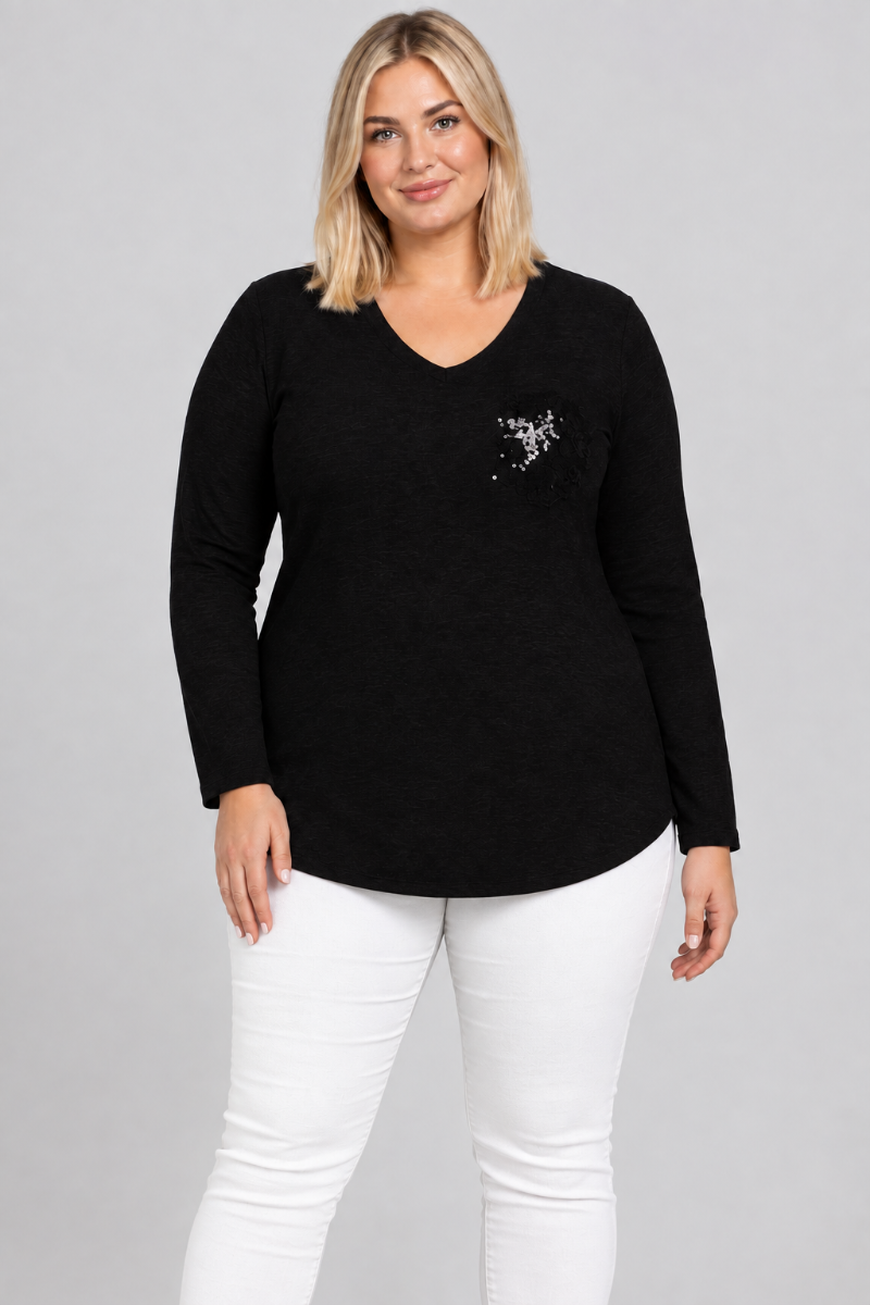 Studio front view of blonde model wearing the black V-neck top with silver embellishment and white pants