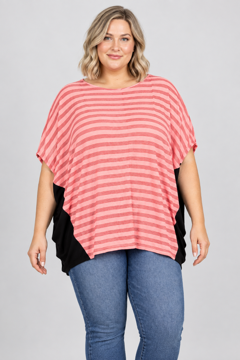 Studio front view of new blonde model in a loose coral-striped top with black side panels and blue jeans