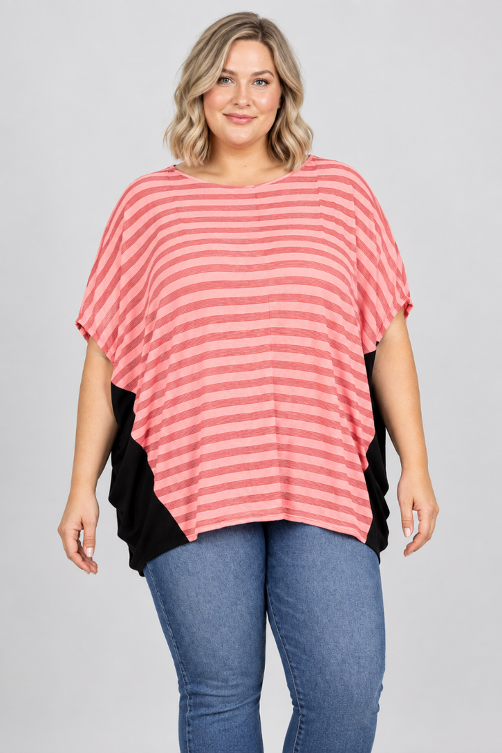 Studio front view of new blonde model in a loose coral-striped top with black side panels and blue jeans