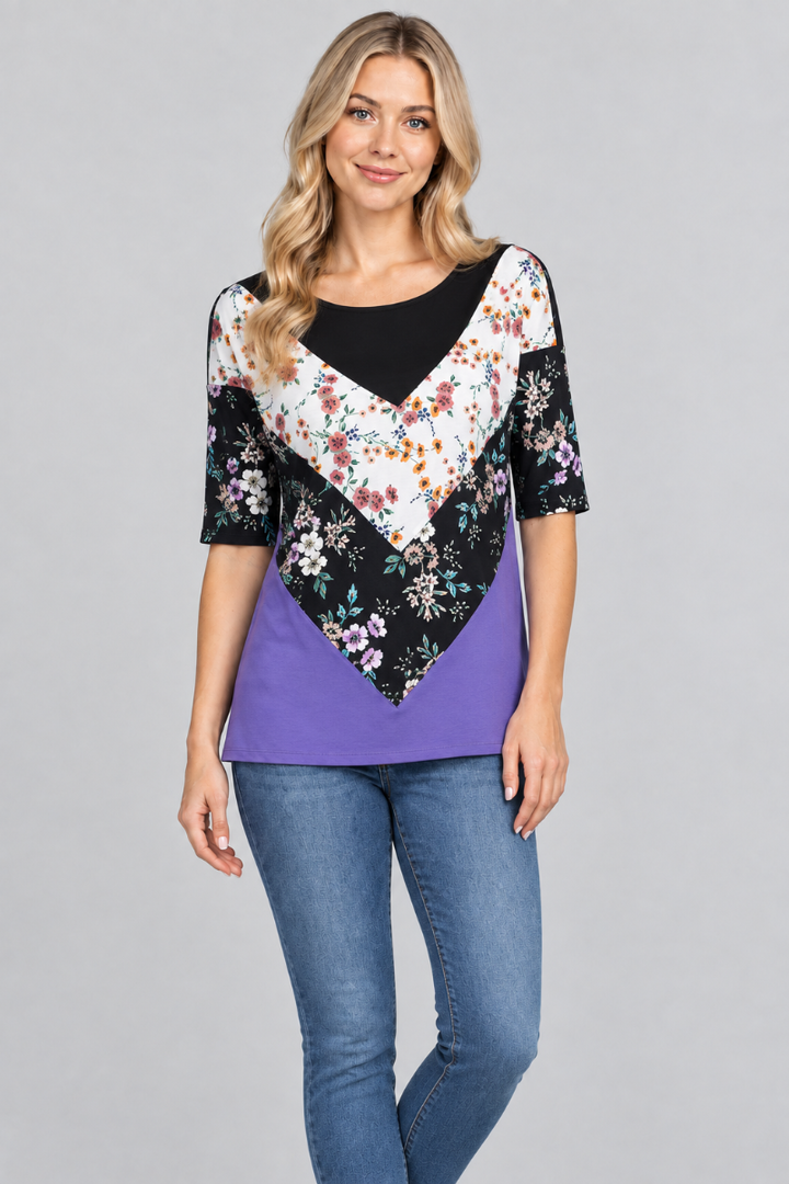 Studio front view of the blonde model wearing the black-and-purple floral top and denim jeans