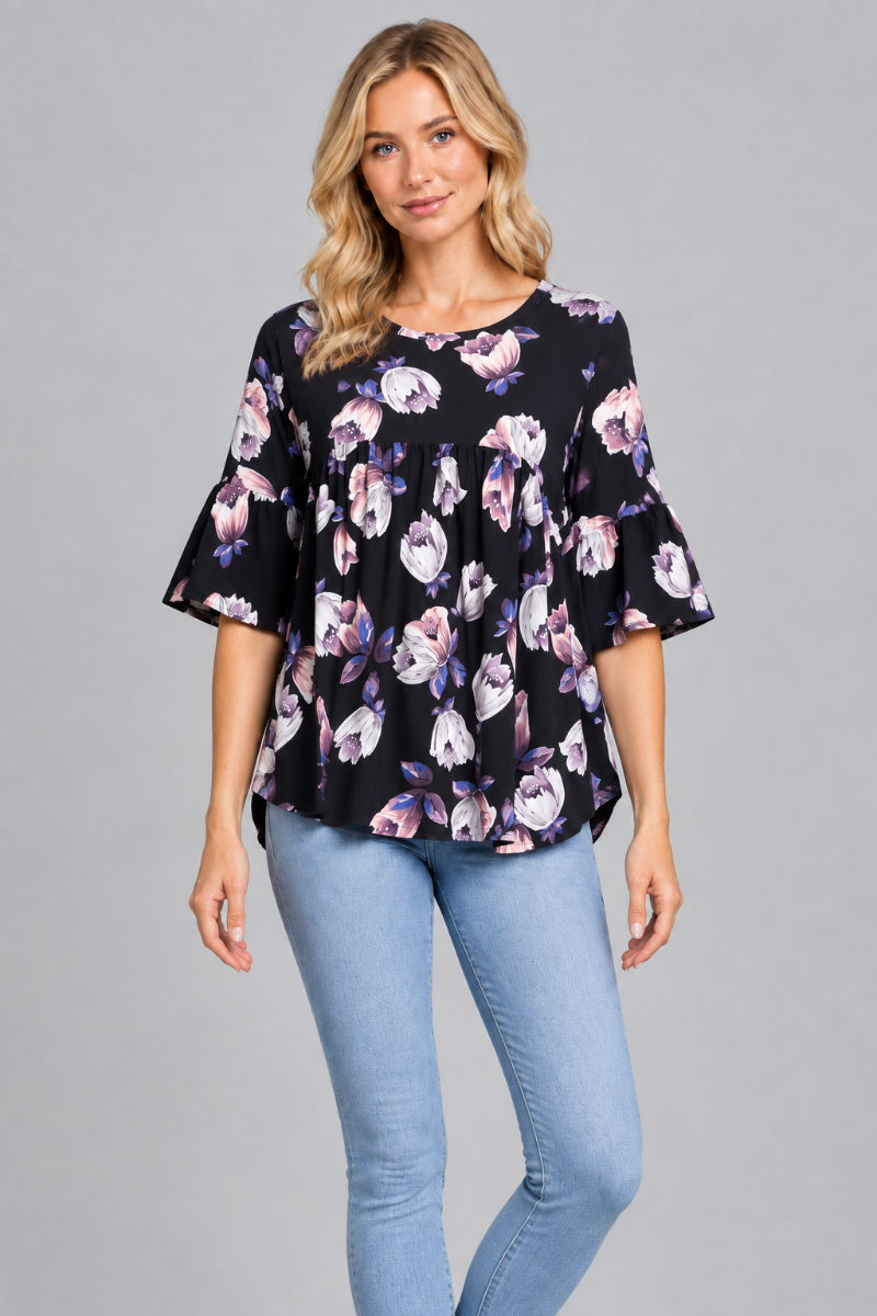 Studio front view of the blonde model wearing the black floral blouse and light-wash jeans