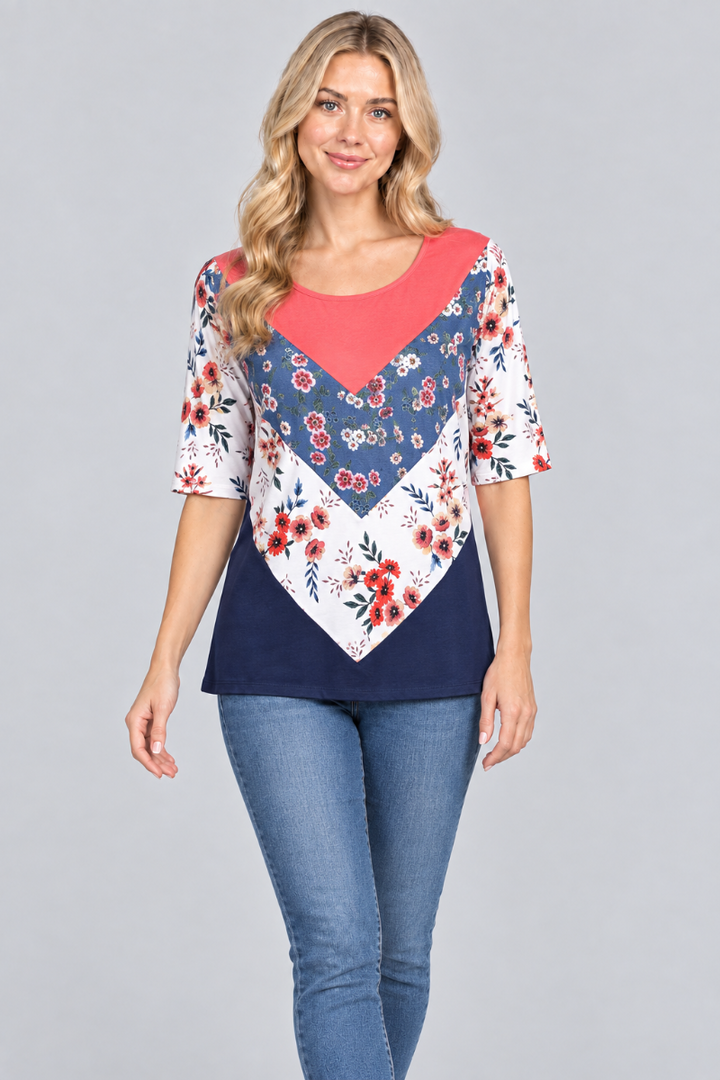 Studio front view of the blonde model wearing the coral-and-navy floral color-block top and denim jeans
