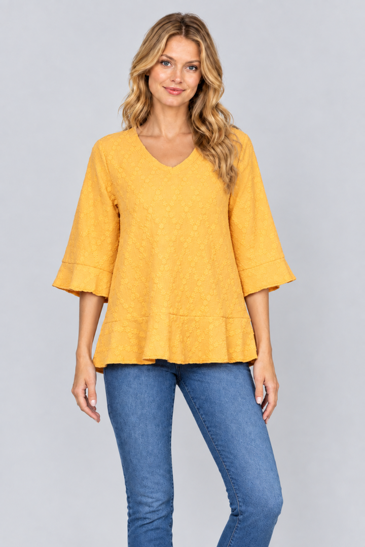 Studio front view of the blonde model wearing the mustard-yellow textured blouse and blue jeans