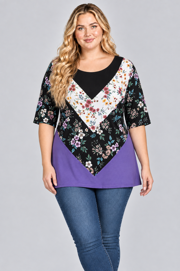 Studio front view of the blonde plus-size model wearing the black, white floral, and purple color-block tunic