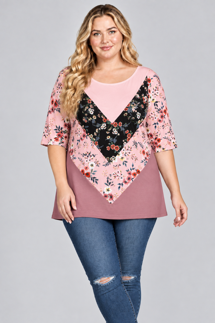Studio front view of the blonde plus-size model wearing the blush-pink, black floral, and dusty rose tunic