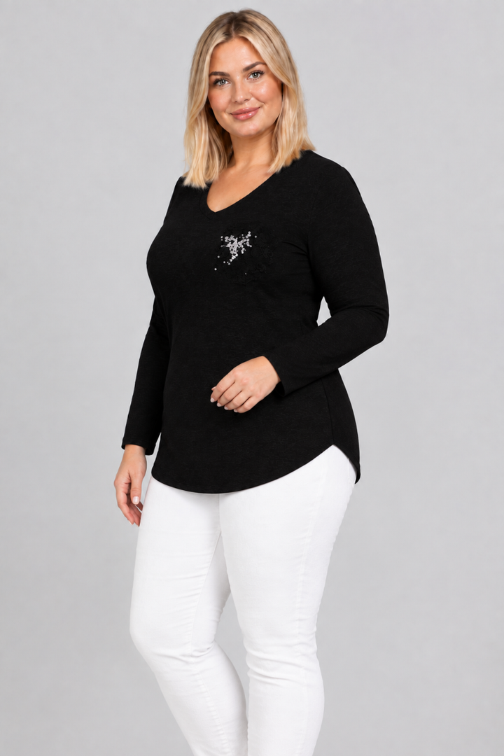 Studio side view of blonde model in black V-neck top with silver embellishment and white pants