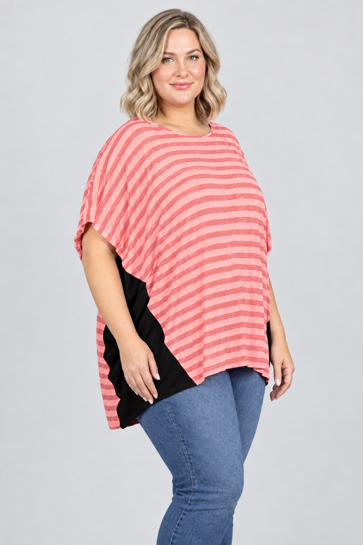 Studio side view of new blonde model in coral-striped dolman top with black side panels and blue jeans