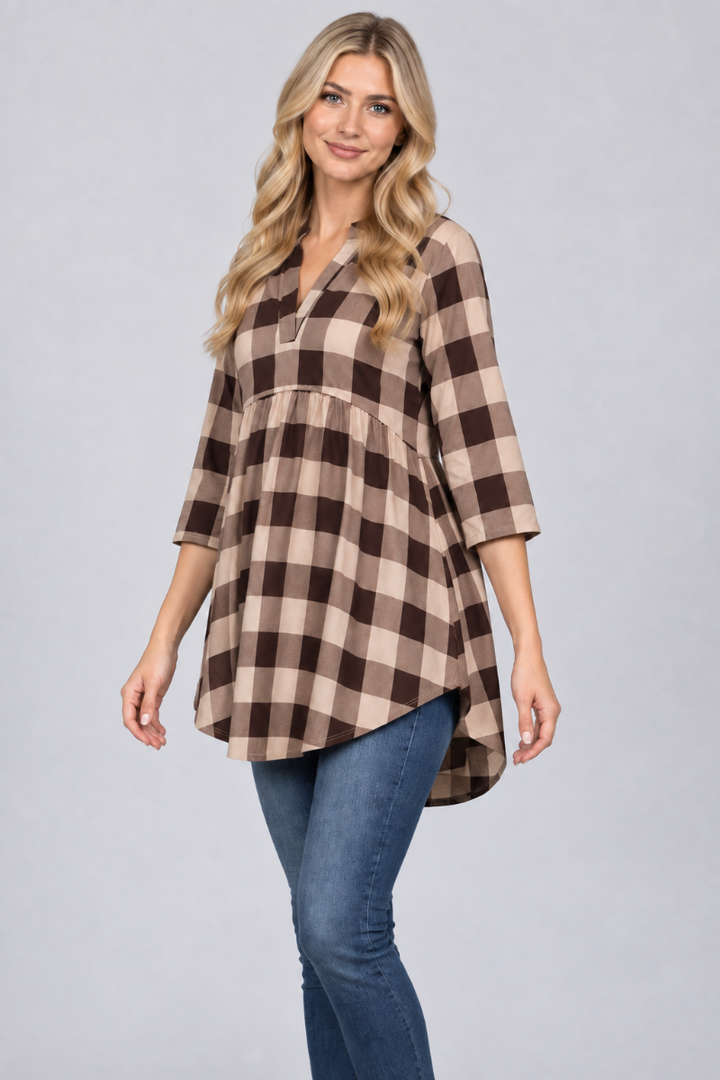 Studio three-quarter view of a blonde model wearing the beige-and-brown plaid tunic and blue jeans