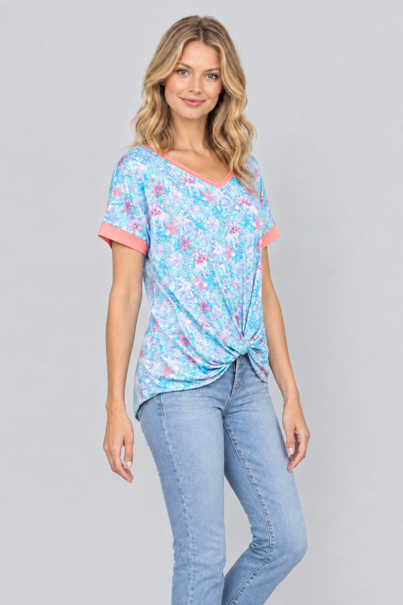 Three-quarter studio view of the blonde model wearing the aqua floral twist-front top and light-wash jeans