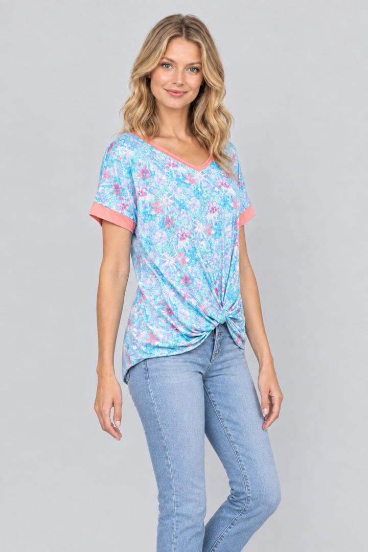 Three-quarter studio view of the blonde model wearing the aqua floral twist-front top and light-wash jeans