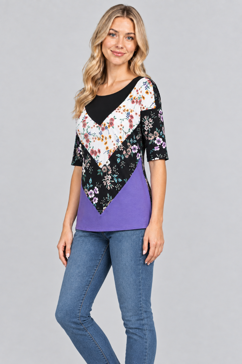 Three-quarter studio view of the blonde model wearing the black-and-purple floral top and denim jeans
