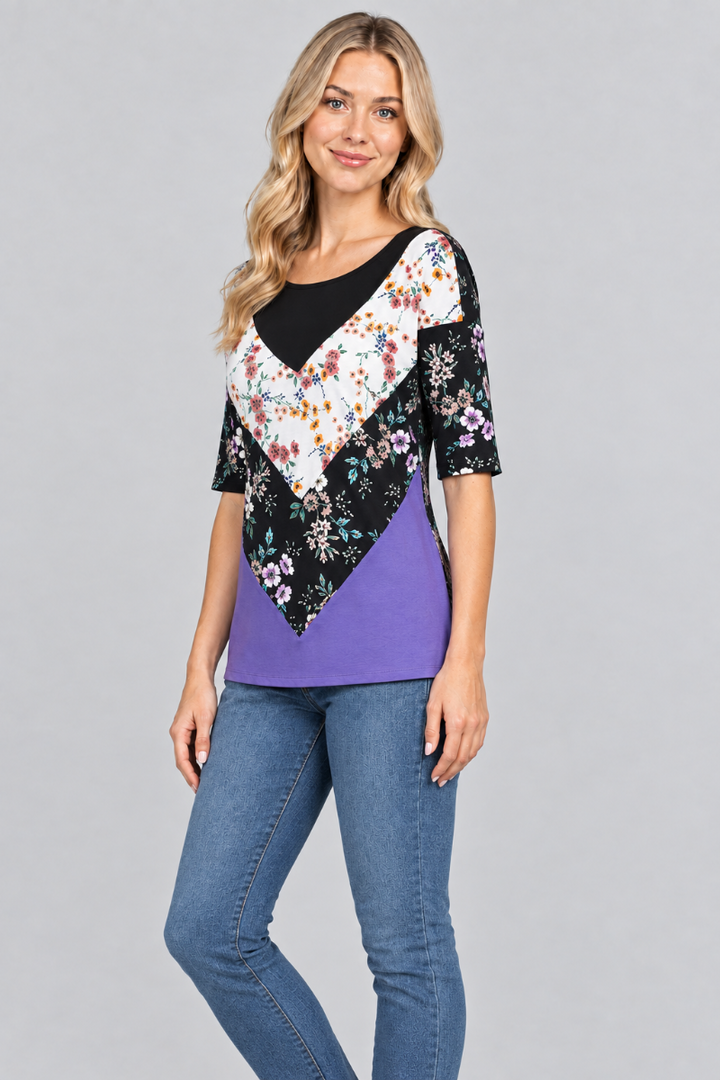 Three-quarter studio view of the blonde model wearing the black-and-purple floral top and denim jeans