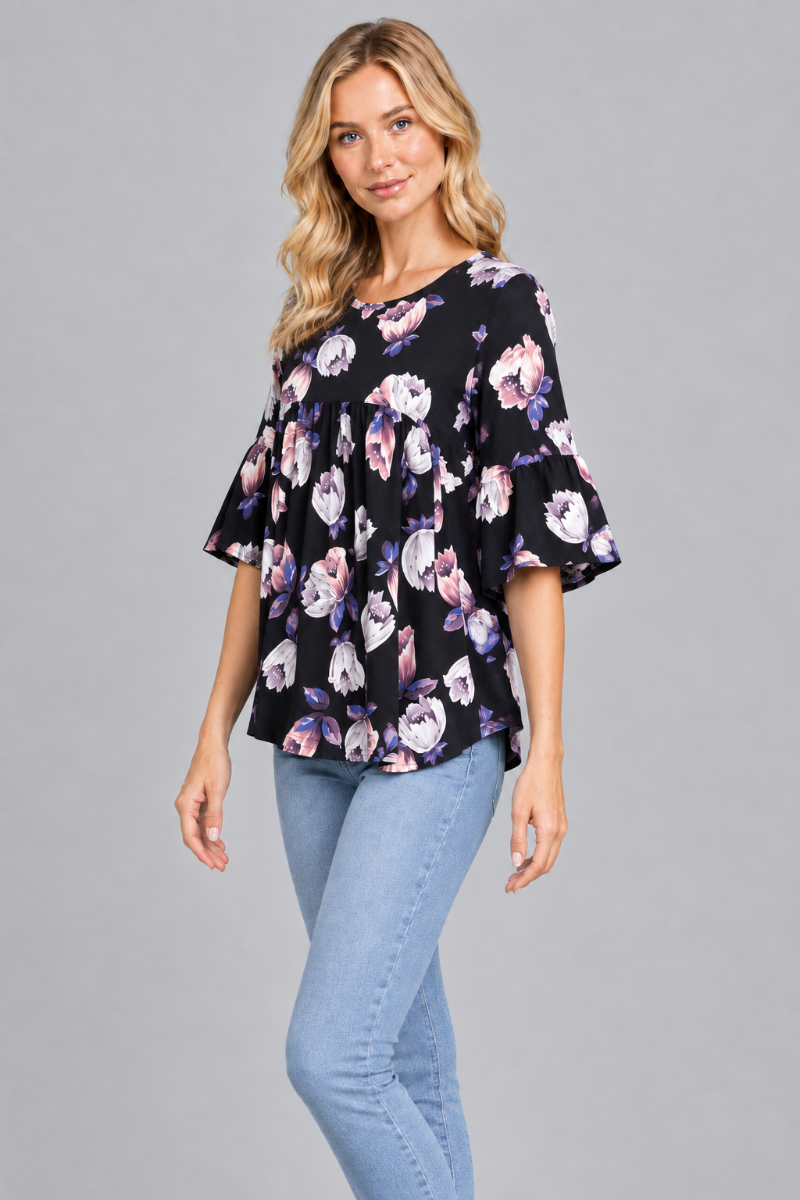 Three-quarter studio view of the blonde model wearing the black floral blouse and light-wash jeans