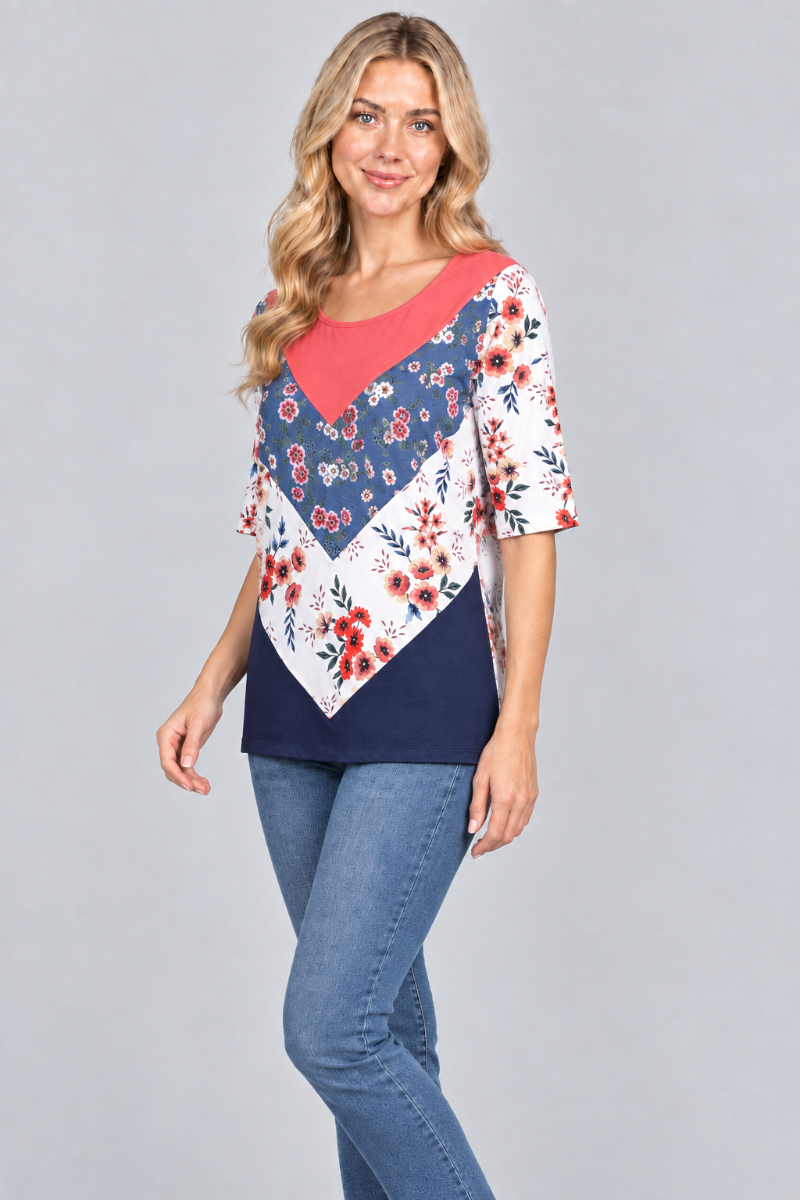 Three-quarter studio view of the blonde model wearing the coral-and-navy floral top and denim jeans