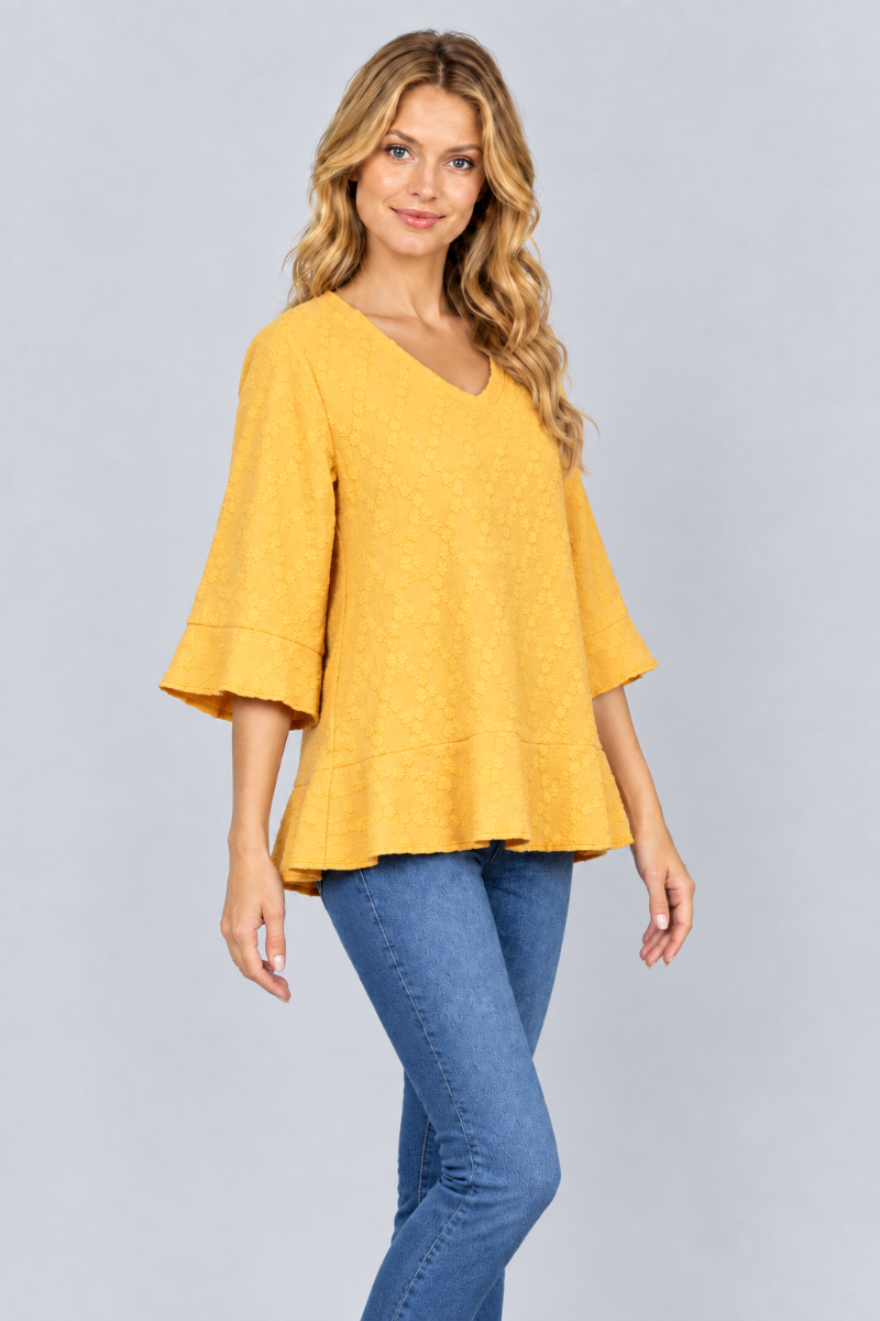 Three-quarter studio view of the blonde model wearing the mustard-yellow textured blouse and blue jeans
