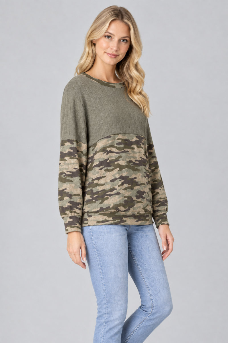 Three-quarter studio view of the blonde model wearing the olive and camouflage color-block top with light-wash jeans