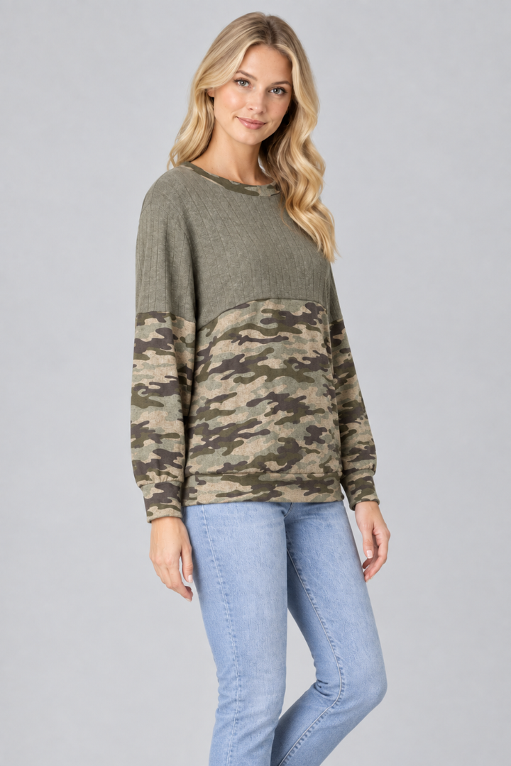 Three-quarter studio view of the blonde model wearing the olive and camouflage color-block top with light-wash jeans