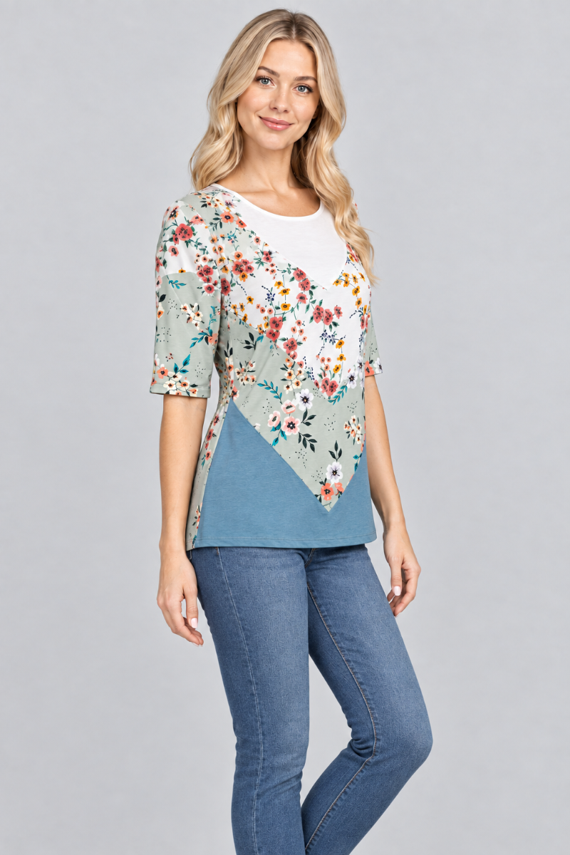 Three-quarter studio view of the blonde model wearing the sage floral and teal top with denim jeans