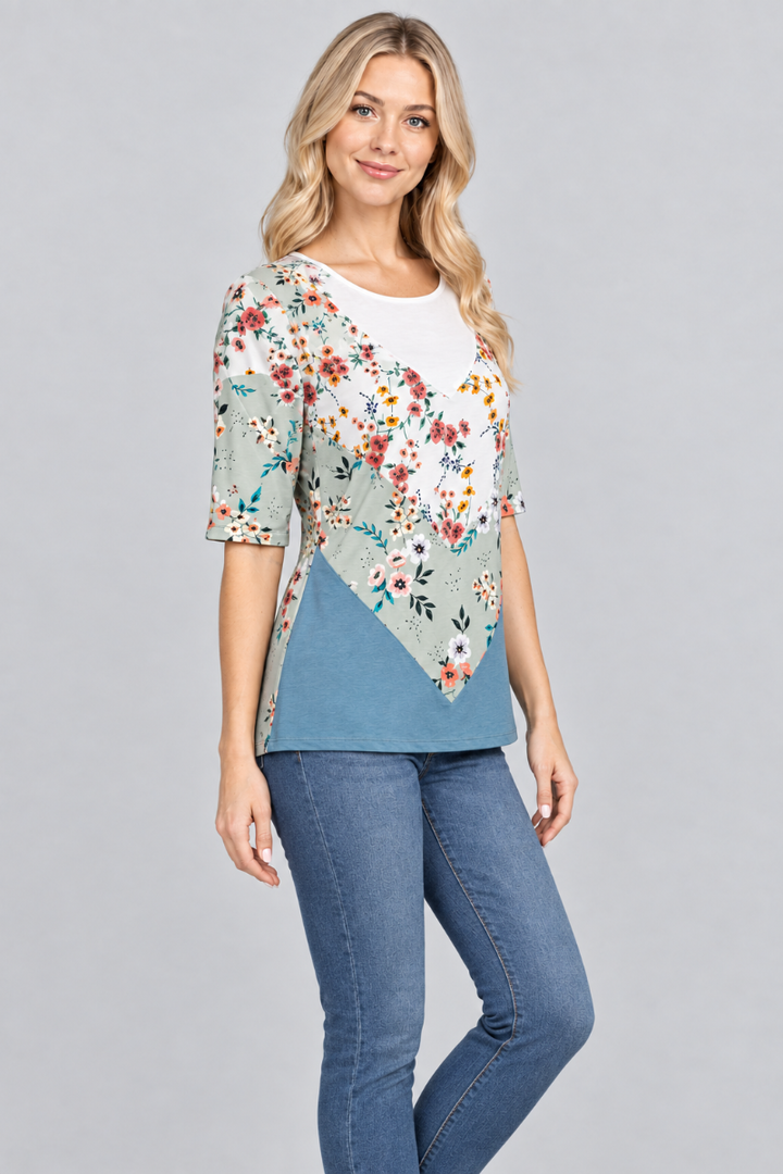 Three-quarter studio view of the blonde model wearing the sage floral and teal top with denim jeans